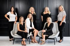 a group of women sitting next to each other in front of a black wall and white chair