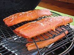 two raw salmons are cooking on the grill