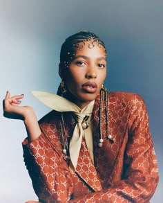 a woman in an orange and white jacket with beads on her head, sitting against a blue background