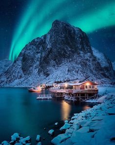 the aurora bore is lit up in the night sky over water and snow covered mountains