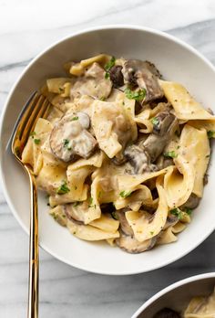 a white bowl filled with pasta covered in mushrooms and parsley next to a fork