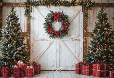 three christmas trees and presents in front of a barn door decorated for the holiday season