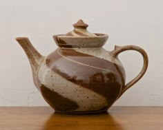 a brown and white ceramic teapot sitting on top of a wooden table next to a wall