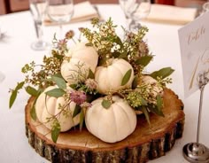 white pumpkins and greenery are arranged on a wood slice at the head table