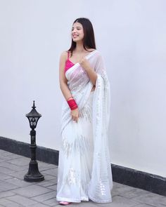 a woman in a white sari standing next to a lamp post