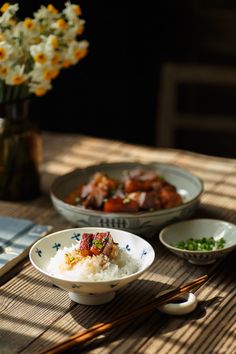 a table topped with bowls filled with rice and meat next to chopsticks on top of a wooden table