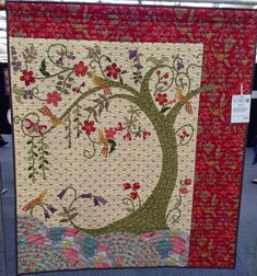 a quilted tree with flowers and birds on it's sides is displayed in the middle of a room