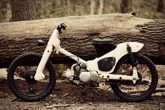 a white and black dirt bike sitting on top of a forest floor next to a fallen tree