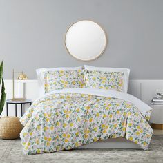 a white bed with yellow and green lemons on it in a room next to a round mirror