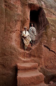 two people are standing in the doorway of a rock formation with steps leading up to them