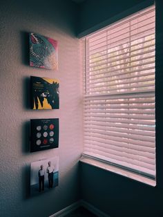 three books are hanging on the wall next to a window with blind shades over it