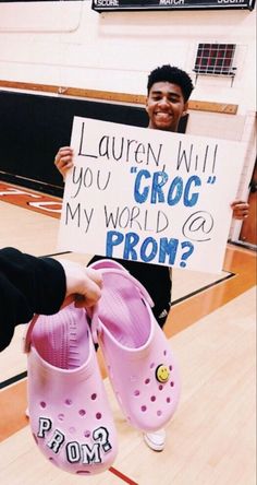 a young man holding up a sign that says, lauren will you croc my world go prom?