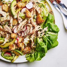 a white plate topped with lettuce and chicken salad next to two silver utensils