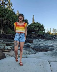 a woman walking on rocks in front of the ocean with her mouth open and tongue out