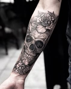 a man with a skull and roses tattoo on his arm is holding the hand of a woman