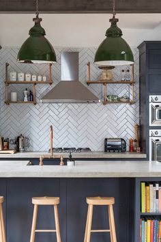 two green pendant lights hanging over a kitchen island with bar stools and bookshelves