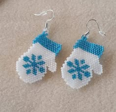 a pair of blue and white beaded snow mitts are hanging from silver earwires