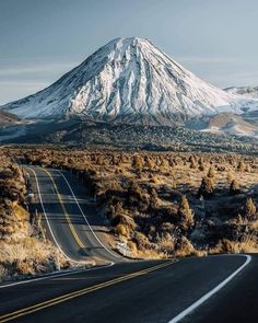 an empty road in the middle of nowhere with a snow covered mountain in the background