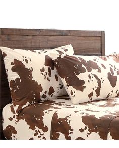 a brown and white cow print bed spread on a wooden headboard with two pillows