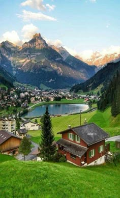 a small village in the middle of a green valley with mountains behind it and a lake on the other side