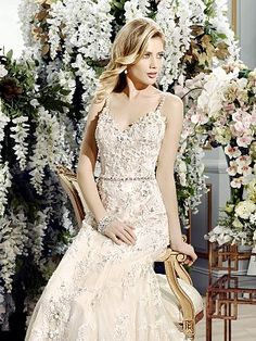 a woman in a wedding dress sitting on a chair with flowers behind her and holding a purse