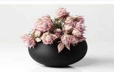 a black vase filled with pink flowers on top of a white table