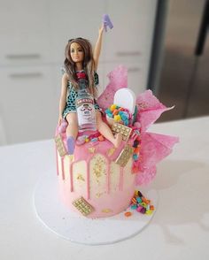 a barbie doll sitting on top of a pink cake with lots of candy and candies