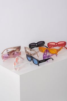 five pairs of sunglasses sitting on top of a white surface, each with different colored frames