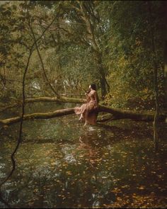 a woman is sitting on a fallen tree in the water