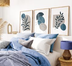 a bed with blue sheets and pillows in a bedroom next to two pictures on the wall