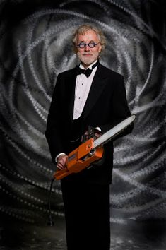 a man in a tuxedo and bow tie holding a piece of wood with an orange object on it