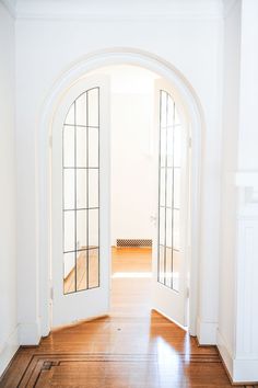 an open door leading into a white room with hardwood floors and arched doors on either side