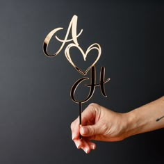 a hand holding a cake topper with the letter a on it and an arrow in the shape of a heart