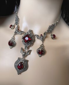 "This hauntingly beautiful Gothic Vampire Bat necklace features antiqued silver plated open winged bats, pendants and filigrees, adorned with dazzling DARK RUBY RED/GARNET glass jewels. Decorated length portion is 6\" wide and 3 1/2\" tall in the center. Necklace is adjustable 15\"-18\" in length. It is worn with soldered stainless steel cable chain and closes with a lobster clasp. If you would like a different length, please send us a message. Matching earrings and headpiece are listed separate Vampire Jewelry Victorian, Vampire Necklace Aesthetic, Red Ruby Victorian Necklace, Red Gothic Gemstone Jewelry, Red Vampire Necklace, Gothic Ruby Necklace, Red Gothic Metal Necklace, Vampire Ring, Vampire Necklace