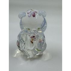 a glass figurine with flowers on it sitting on a white surface, in the shape of a bear