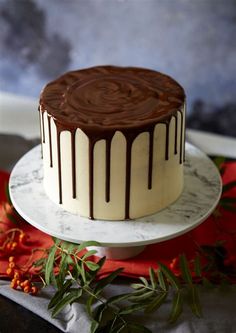 a chocolate cake with white frosting on a plate next to red flowers and greenery