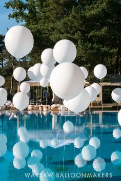 balloons floating in the air near a pool with a teddy bear sitting on top of it