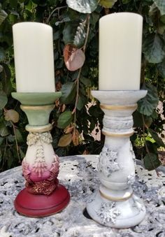 two candles sitting on top of a table next to each other with leaves in the background