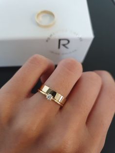 a woman's hand with a gold ring on top of it and a white box in the background