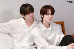 two young men sitting next to each other on top of a white bed covered in pillows