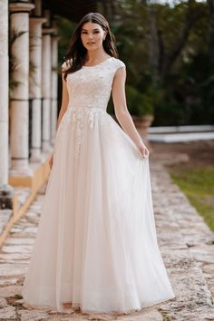 a woman in a white wedding dress standing on a stone walkway with columns behind her