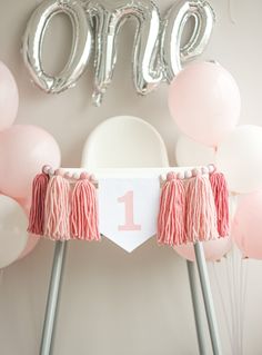 a pink and white 1st birthday party with balloons, tassels, and decorations