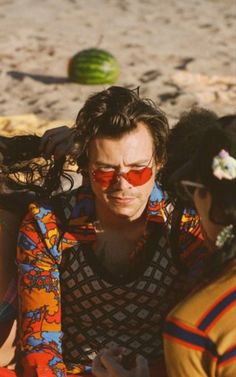 two people sitting on the beach with one wearing red sunglasses and the other in yellow