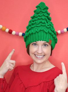 a woman wearing a green knitted christmas tree hat and giving the thumbs up sign