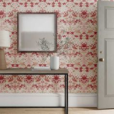 a room with a table and lamp next to a wallpapered wall that has red flowers on it