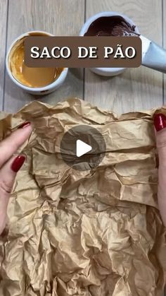 two hands holding brown paper over a wooden table with sauces and spoons on it