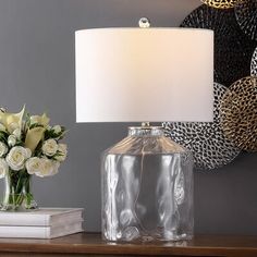 a lamp on a table next to a vase with white flowers and a mirror behind it