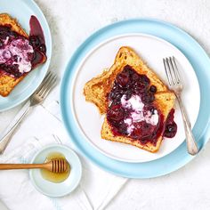 two pieces of toast with blueberry compote and butter on white plates next to silverware