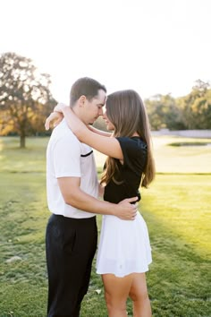 a man and woman standing in the grass with their arms around each other as they kiss