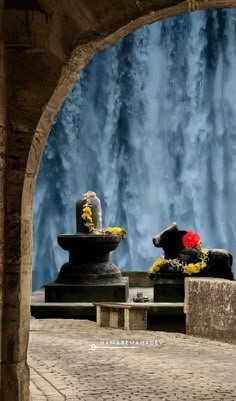 two statues with flowers on them in front of a waterfall